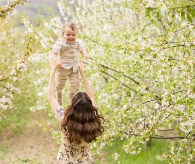 Güzel genç anne oğluyla bahar bahçesinde oynuyor. Köyde tatil.