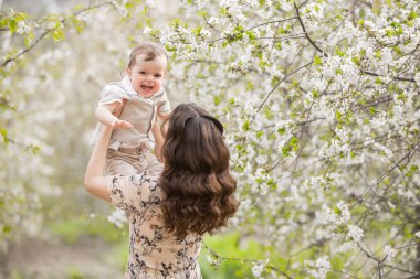 Güzel genç anne oğluyla bahar bahçesinde oynuyor. Köyde tatil.