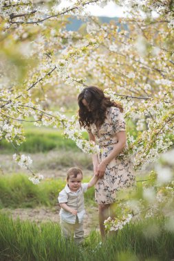 Güzel genç anne oğluyla bahar bahçesinde oynuyor. Köyde tatil.