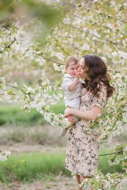 Güzel genç anne oğluyla bahar bahçesinde oynuyor. Köyde tatil.