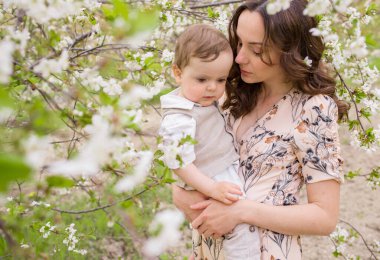 Güzel genç anne oğluyla bahar bahçesinde oynuyor. Köyde tatil.