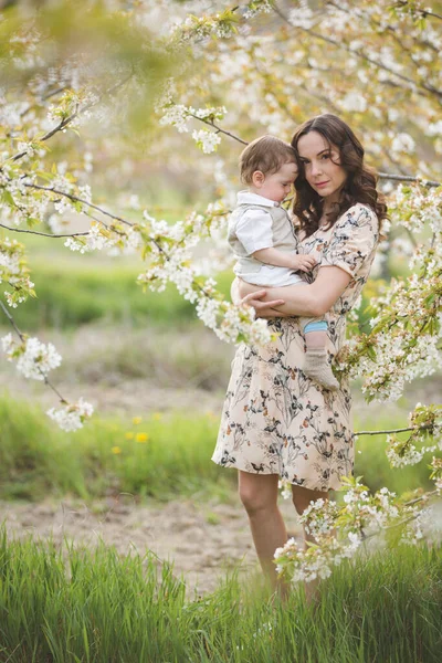 美しい若いお母さんは春の庭で息子と遊ぶ 村での休日 — ストック写真