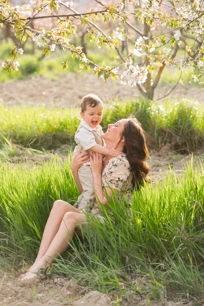 美しい若いお母さんは春の庭で息子と遊ぶ 村での休日 — ストック写真