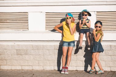 İki kız kardeş ve erkek kardeşleri vaiel bardağında dondurma yiyorlar. Ergenler şık giyinir. Sokak manzarasına karşı poz veren çocuklar