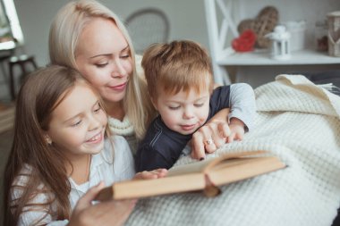 Kendini izole etme döneminde olan aile evde kanepede kitap okuyor. Evinizi terk etmeden karantina sırasında kendinizi nasıl meşgul edersiniz?