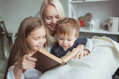 Kendini izole etme döneminde olan aile evde kanepede kitap okuyor. Evinizi terk etmeden karantina sırasında kendinizi nasıl meşgul edersiniz?