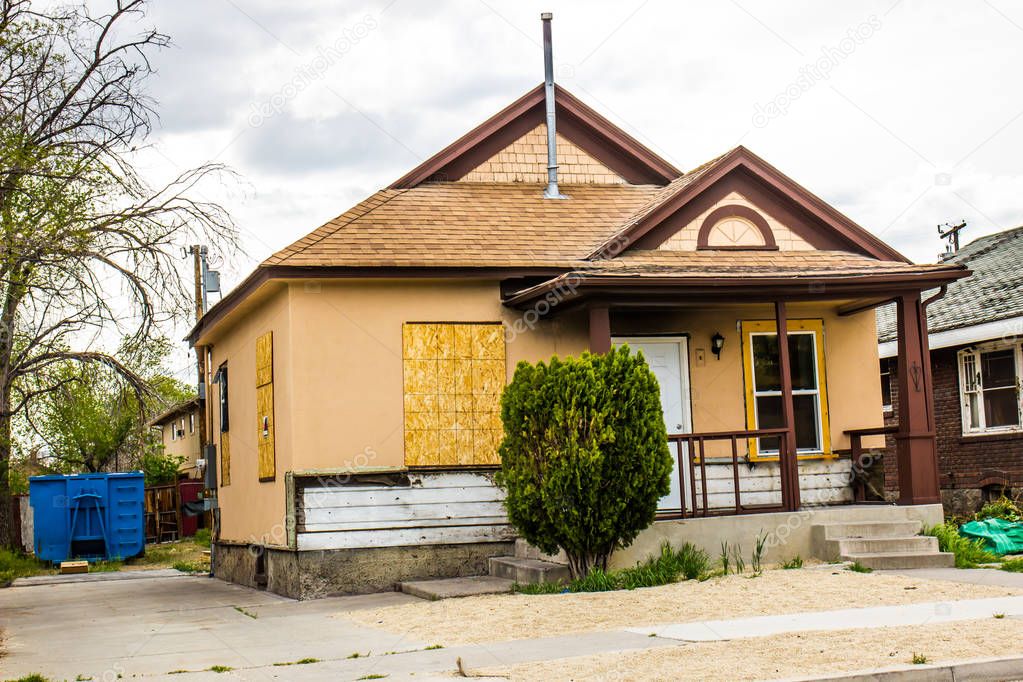 Abandoned One Level Home With Boarded Up Windows And Trash Dumpster