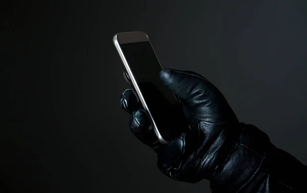 Злочинець тримає смартфон з чорними шкіряними рукавичками в темряві. Хакер торкається екрана смартфона . — стокове фото