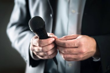 Stage fright concept. Nervous and shy public speaker with microphone. Business man afraid of giving speech for crowd of people or audience. Sweaty hands holding mic. Bad presentation. Stressed singer. clipart