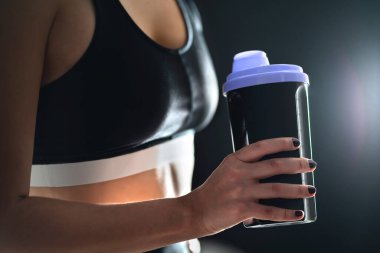 Egzersiz ve beden eğitiminden sonra protein içeceği. Elinde bir şişe spor içeceği tutan sağlıklı bir kadın. Sütlü mü, sulu mu? Titreşimli fitness sporcusu. Egzersiz sonrası iyileşme için içme takviyesi.
