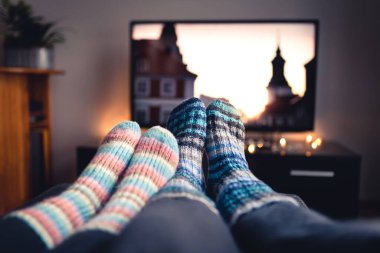 Çoraplı ve yün çoraplı bir çift kışın TV 'de film veya dizi seyrediyor. Oturma odasındaki kanepede birlikte oturan ya da uzanan kadın ve erkek televizyondaki çevrimiçi yayın servisini kullanıyor.