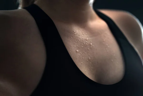 Sweat on skin. Sweaty woman after gym workout, heavy cardio or fat burning training. Yoga instructor, tired fitness athlete or personal trainer. Low key close up of wet female chest with water drops.