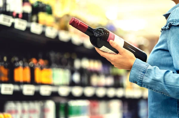 酒类商店或超市的酒精货架 女人在商店里买了一瓶红酒和酒精饮料 快乐的女性顾客选择了美乐或者桑乔维斯 购物精神的概念 — 图库照片