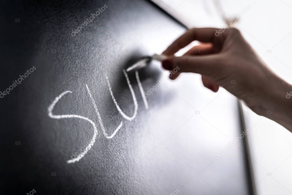 Bullying concept. Mean hate comment and rumour written on chalkboard in school classroom. Sexual harassment. Bully writing insult on blackboard. Student or teacher being bullied. Bad behavior.