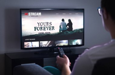 Akıllı TV 'de çevrimiçi film yayını. Televizyonda talep videosu (VOD) ile yayınlanan dizi. Uzaktan izlemek için filmi seçen adam. Gece geç saatte evdeki kanepede oturan kişi..
