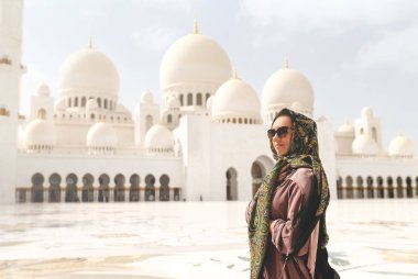 Şeyh Zayed 'in Büyük Camii' ndeki mutlu kadın. Adu Dabi 'de türbanlı ve elbiseli bir kadın turist. Abu Dabi, BAE 'de güzel bir İslami dekor ile geleneksel Müslüman binasında yürüyen bir kadın..