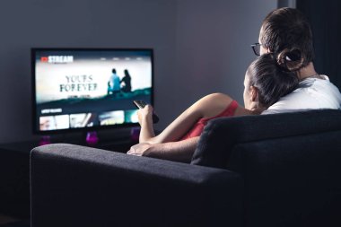 Akıllı televizyondaki film yayını servisi. İnternette bir çift dizi izliyor. Kadın uzaktan kumandalı yeni sezonu ya da filmi seçiyor. İstenildiğinde video (VOD) site modeli ekranda. Dijital yayın ağı.