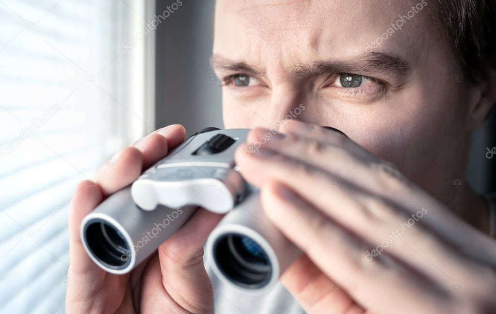Man with binoculars. Private detective, agent or investigator looking out the window. Man spying or investigating. Privacy, surveillance or espionage concept. Suspicious or curious person spying.