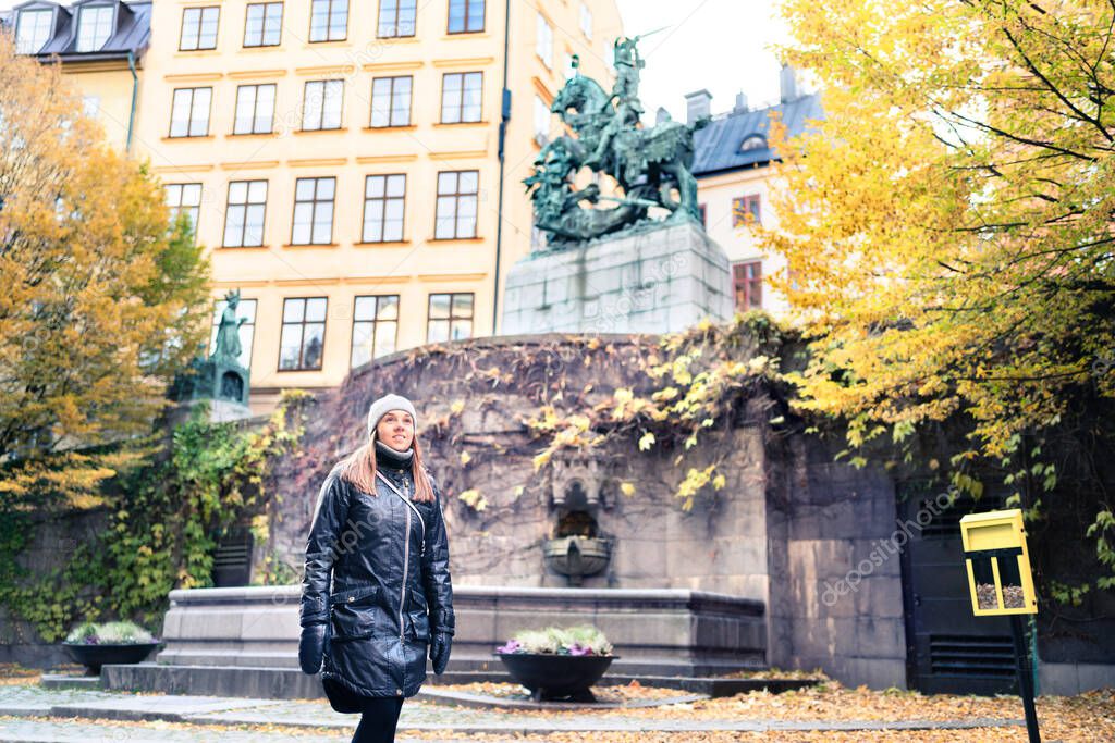 Person walking in Stockholm and old town (Gamla Stan) in winter or autumn. Yellow fall colors in trees and leafs. Woman on vacation in Sweden in Scandinavia. Beautiful happy tourist in Swedish city.
