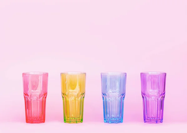 Multi-colored glasses for drinks on a pink background. Minimastic composition. Glasses of glass.