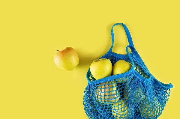 Blue string bag with apples on a yellow background.