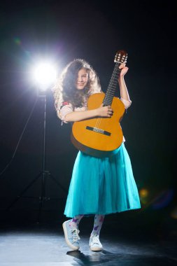 Kıvırcık saçlı ve mavi elbiseli komik küçük kız sahnede gitar çalar ve güler. Genç yetenekler kavramı