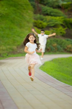 Bir kız ve bir oğlan yol boyunca koşup kovalamaca oynuyorlar. Çocuk oyunları ve açık hava aktiviteleri.