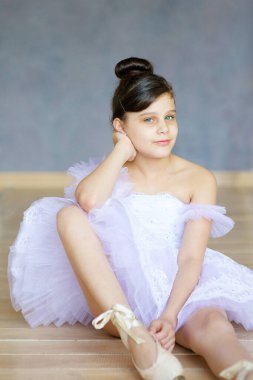 Beyaz etekli küçük kız balerin bale sınıfında yerde oturuyor..