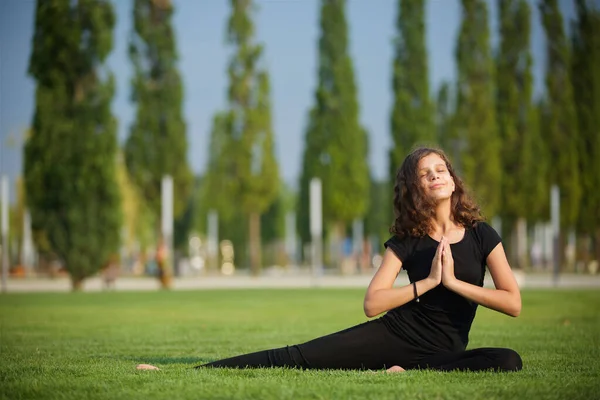 Girl doing yoga school age in sports form shows the elements of sports and asanas. Open Park area. The concept of sport and healthy lifestyle.