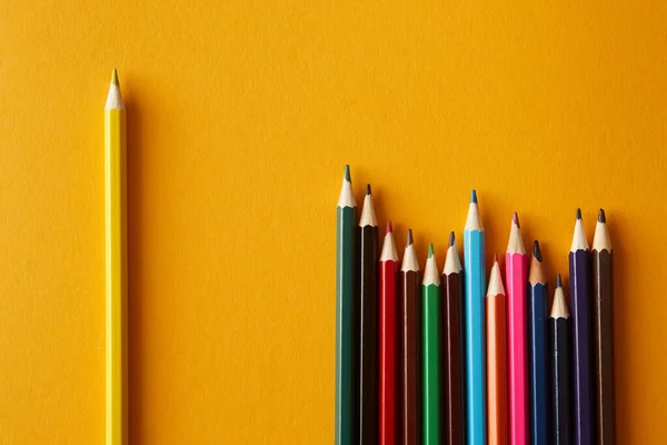 A set of colored pencils on a bright yellow background. One yellow pencil is placed separately. The concept of individuality and selectivity.