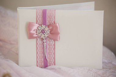 Düğünde yeni evliler için beyaz kapalı dilek kitabı. Masada pembe kurdeleler ve dantellerle süslenmiş..