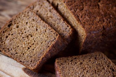 Bir somun siyah çavdar ekmeği ahşap bir masada yatıyor. Ekmek parçalara bölündü..
