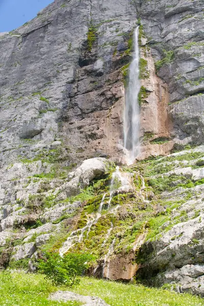 Mountain waterfall with clean water falls from a small height. Around green grass.