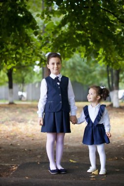 Sevimli birinci sınıf öğrencisi, yılın ilk okul günü şirin kız kardeşinin elini tutuyor.