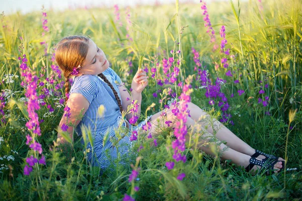 夏に草の上に花のある畑に座っている女の子 — ストック写真