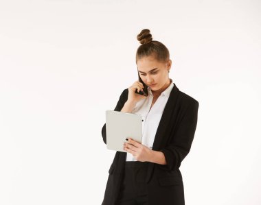 Ofis tarzı bir kız telefonda konuşuyor ve temiz beyaz bir arka planda çekilmiş bir tablete bakıyor. İş kadını kavramı..