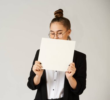 Ofis kıyafetleri içinde genç bir kız elinde beyaz boş bir kağıt tutuyor. Reklam ve metin için kullan.