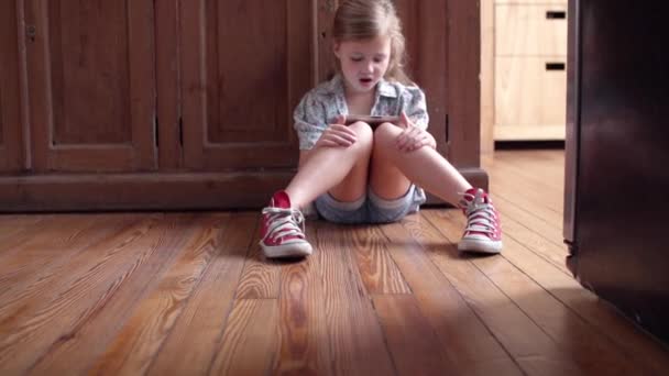 Petite fille assise sur le sol, regardant la tablette numérique et chantant — Video