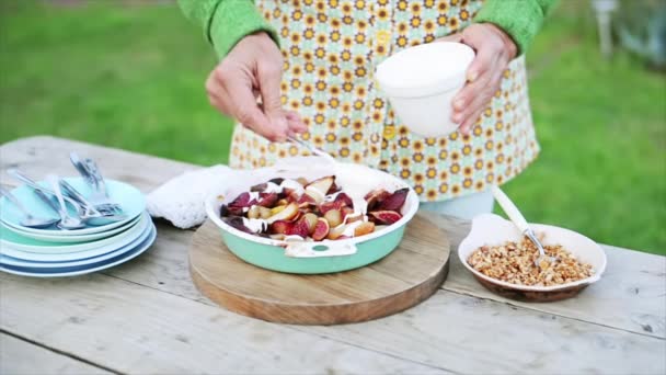 Mujer poniendo crema y nueces picadas en postre de frutas — Vídeo de stock