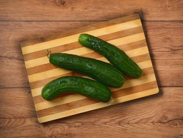Pile of green cucumbers on wooden cutting board — Stock Photo, Image