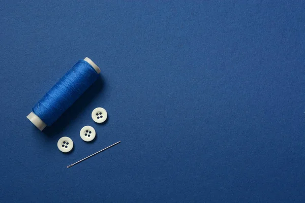 Blue cotton thread, sewing buttons and tailor needle - blue back — Stock Photo, Image