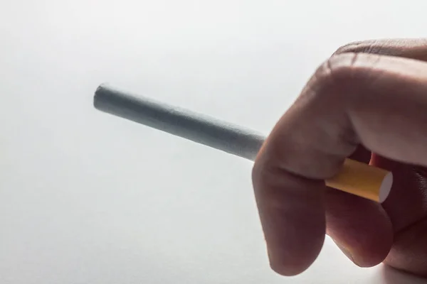 Primo piano di una mano che tiene una sigaretta su sfondo bianco — Foto Stock