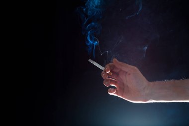 karanlık bir ortamda dumanlı bir sigara tutan el
