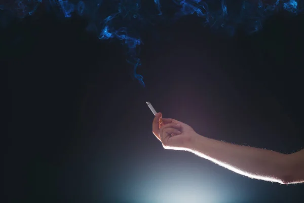 Mano che tiene una sigaretta fumosa in un'atmosfera buia — Foto Stock