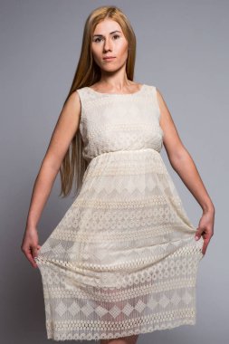 stüdyoda gri bir arka plan üzerinde beyaz elbiseli genç sarışın