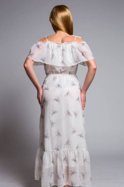 stüdyoda gri bir arka plan üzerinde bir desenli beyaz elbiseli genç sarışın