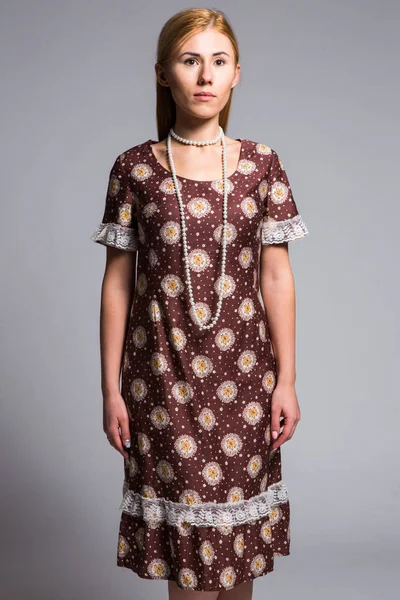 Jovem loira em um vestido vintage marrom com um padrão abstrato em um fundo cinza no estúdio — Fotografia de Stock