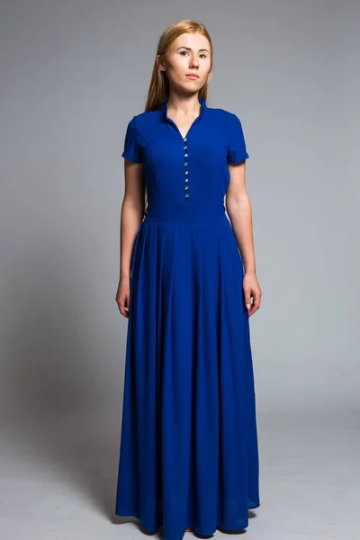 Νεαρή ξανθιά σε ένα μπλε φόρεμα σε γκρι φόντο στο στούντιο — Φωτογραφία Αρχείου