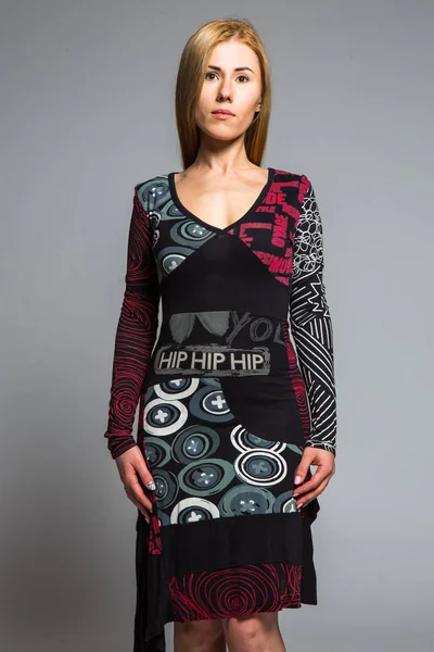 Jovem loira em um vestido com um padrão abstrato em um fundo cinza no estúdio — Fotografia de Stock