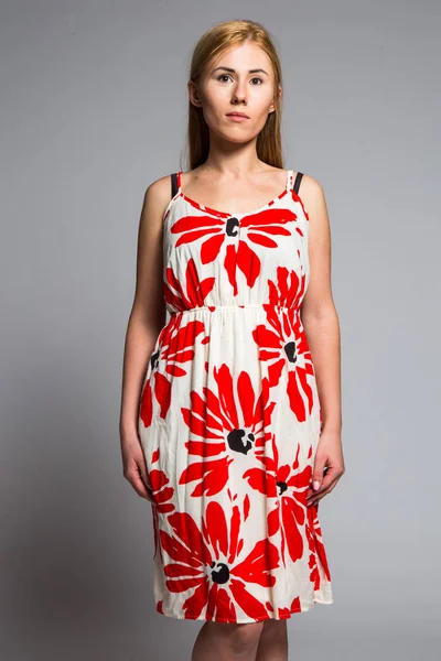 Молода блондинка в білій сукні з червоним квітковим візерунком на сірому фоні в студії — стокове фото